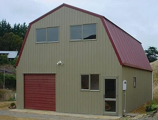 Two-story barn-style building with red roof and garage door; beige siding, windows, and a doorway.