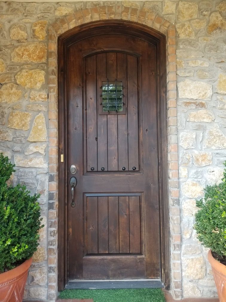 A wooden door is surrounded by potted plants in front of a stone wall.