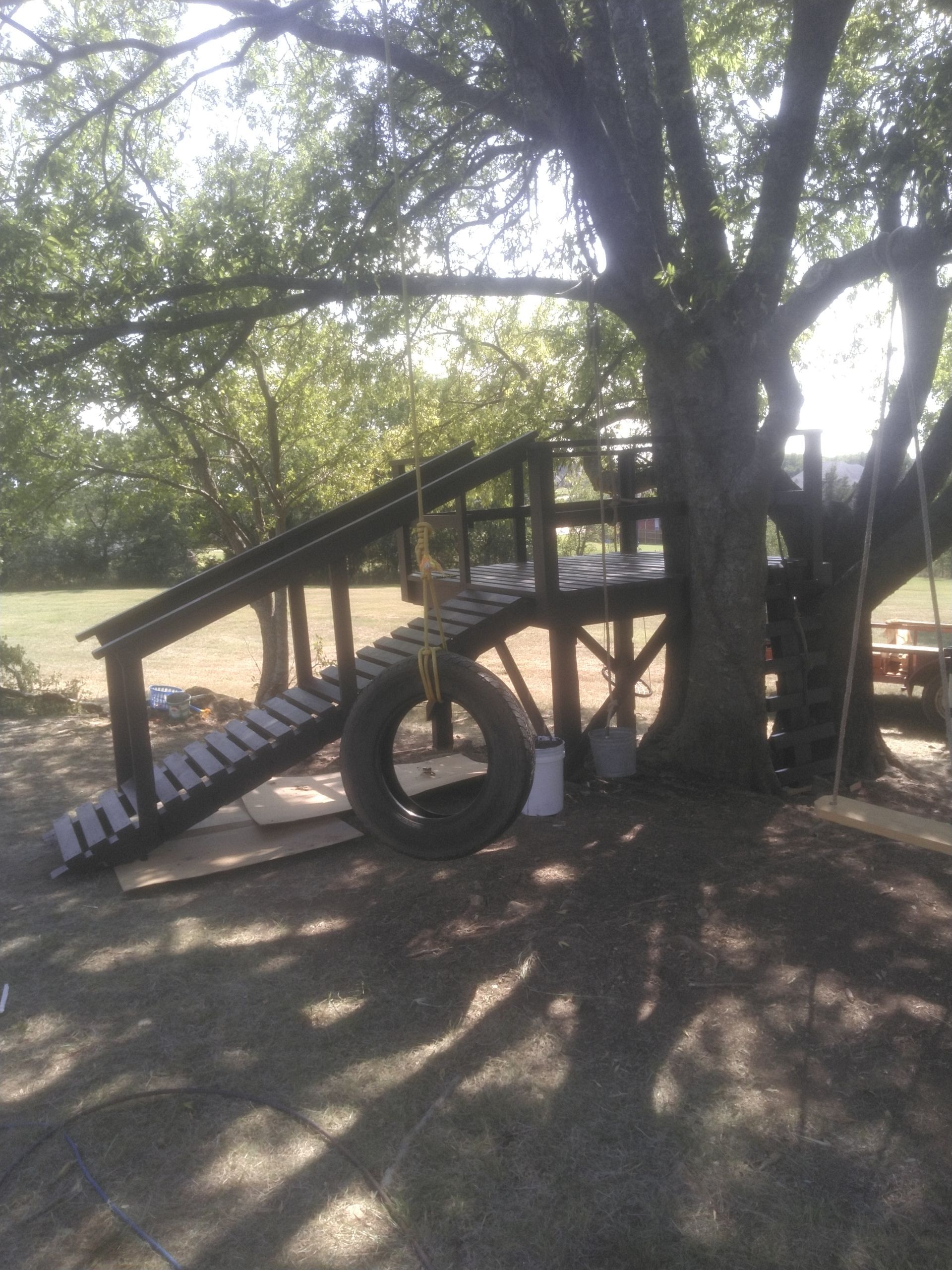 A playground with a tire and stairs under a tree