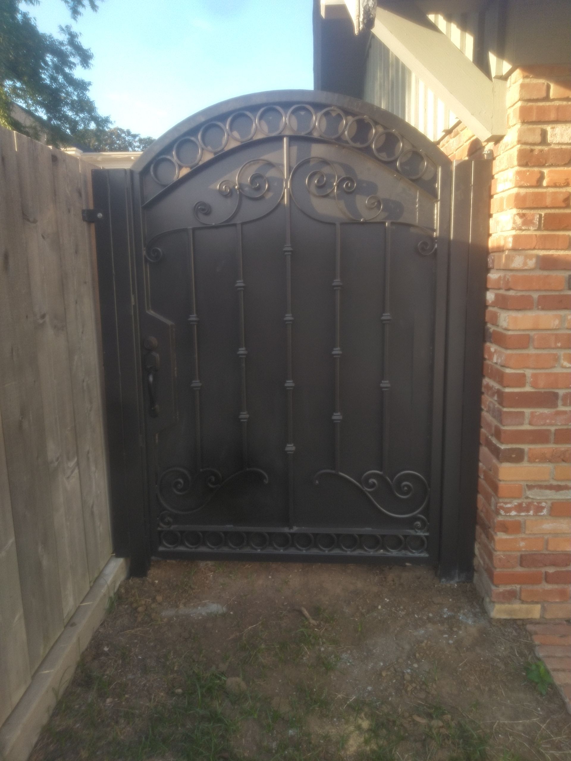 A black wrought iron gate is next to a brick wall