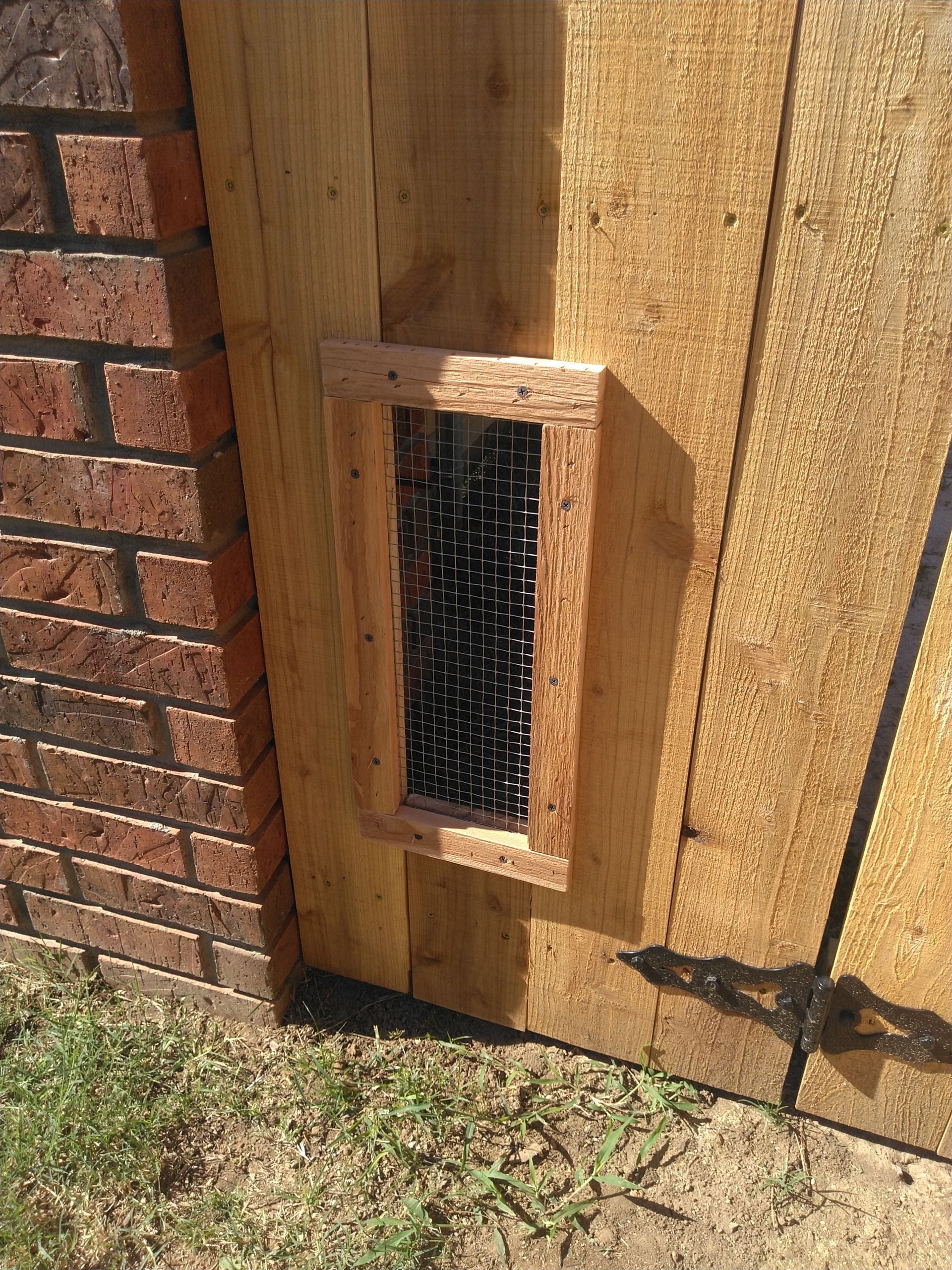 A wooden gate with a hole in it next to a brick wall.