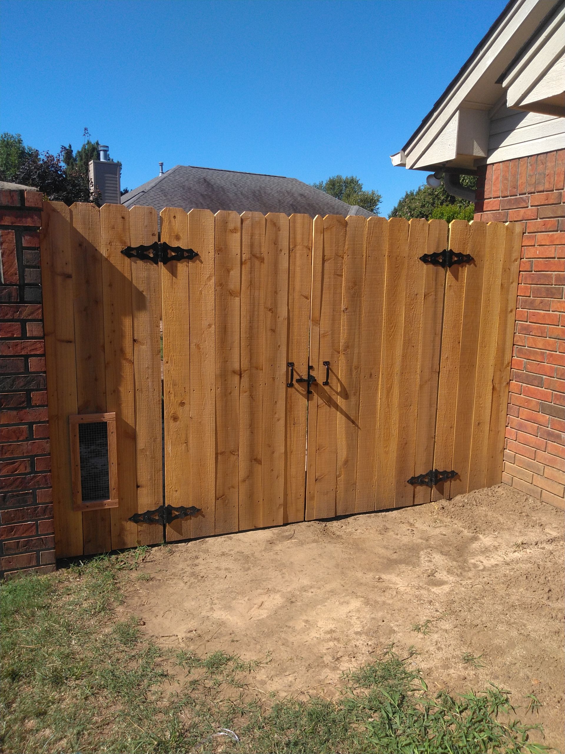 A wooden fence with a dog door in the backyard of a house.