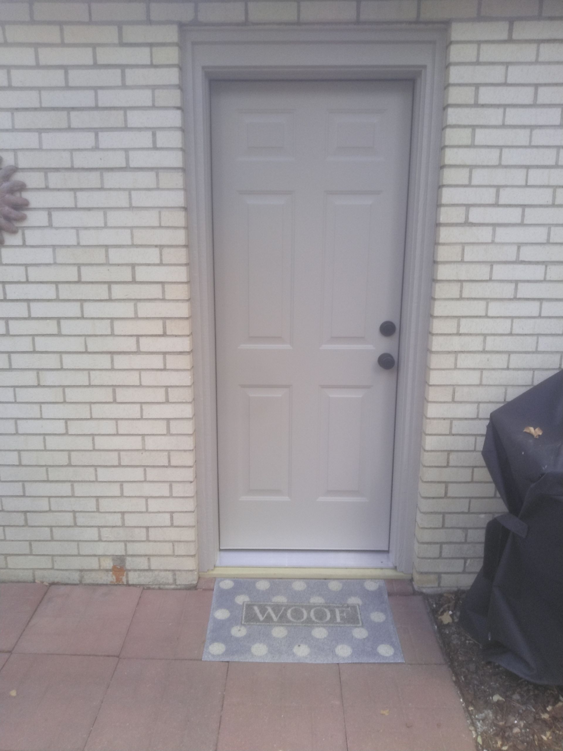 A white door is sitting on a brick wall next to a door mat.