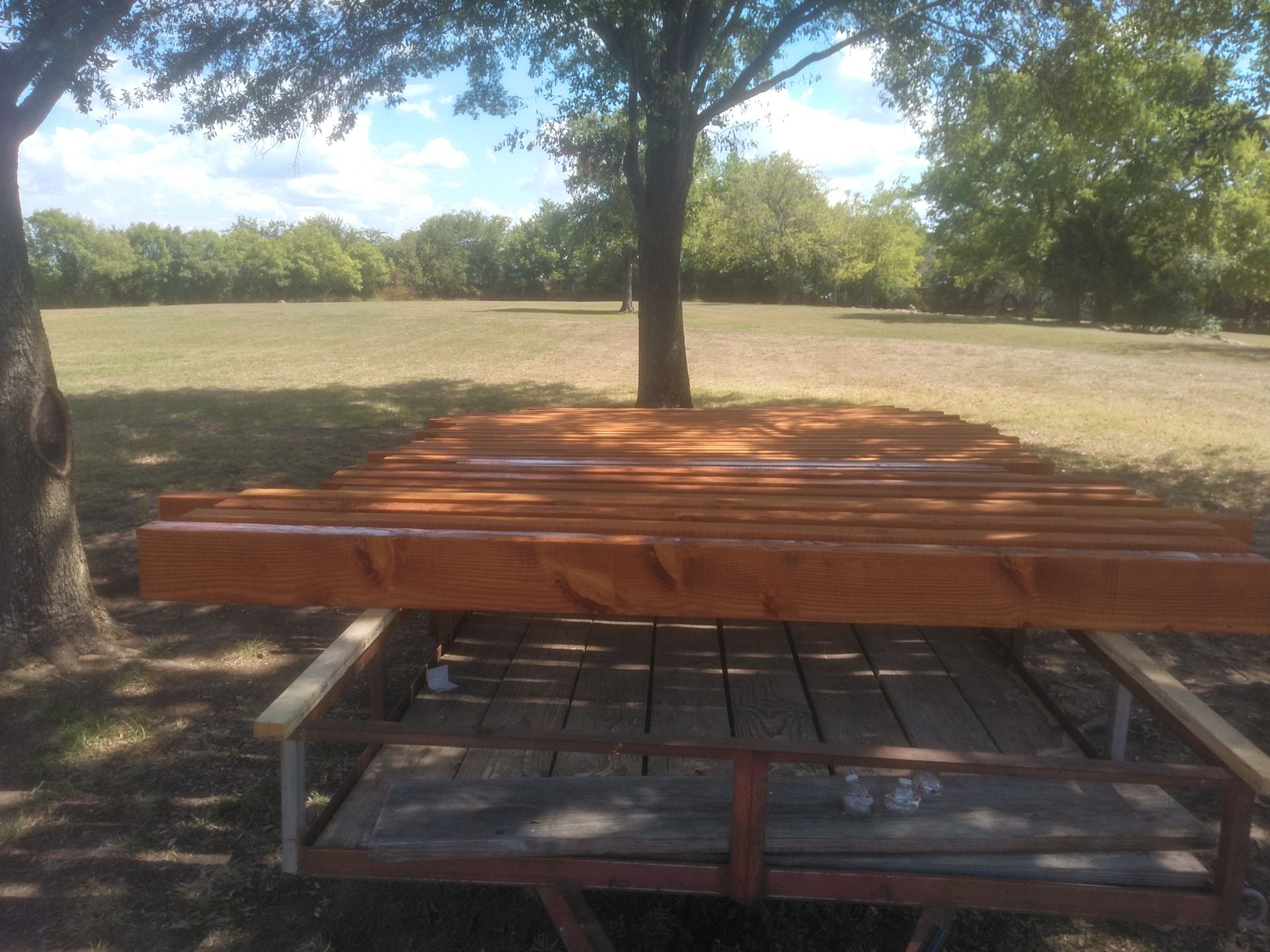 A wooden picnic table is sitting under a tree in a field.
