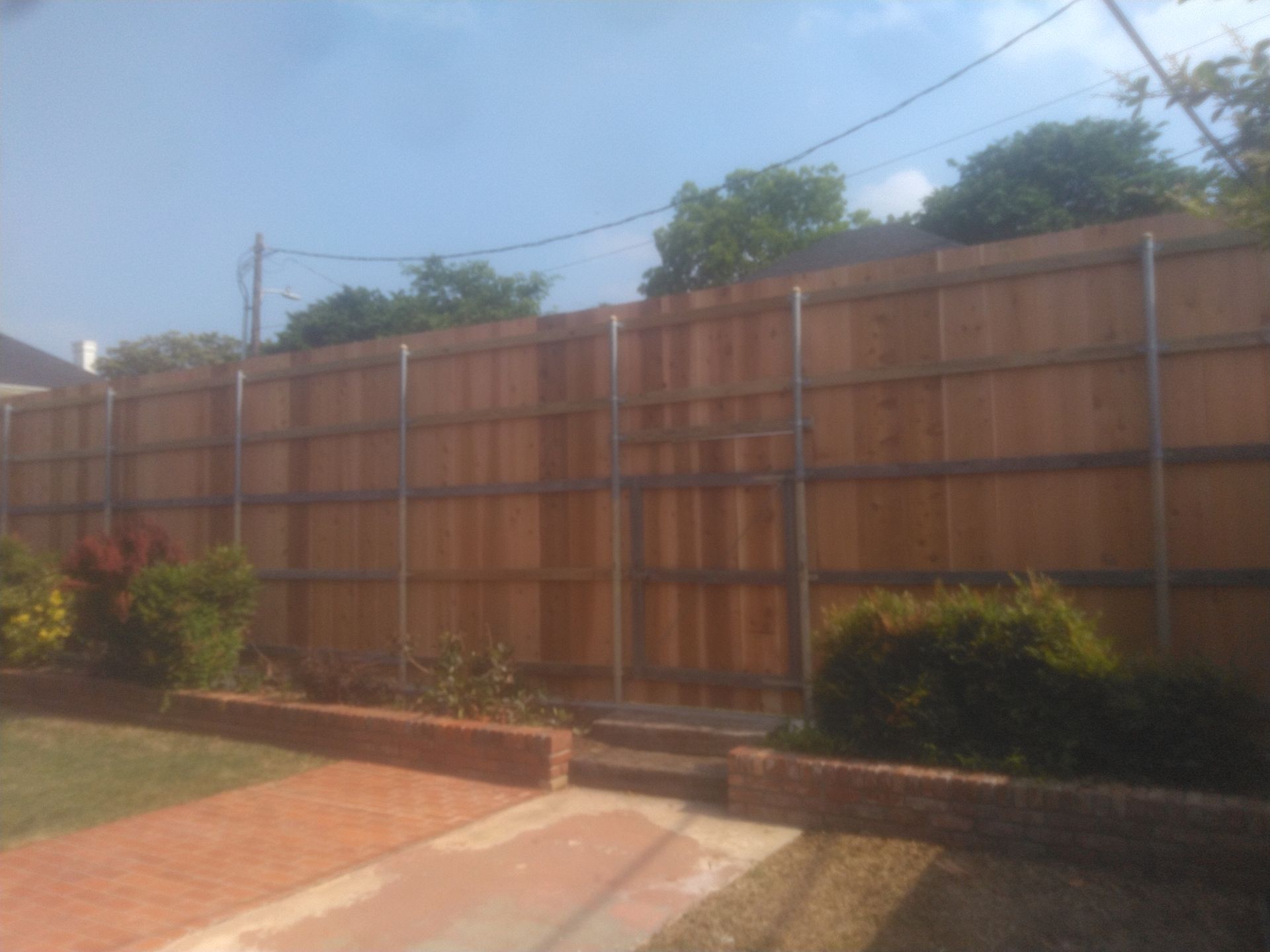 A wooden fence is surrounding a brick driveway in a backyard.