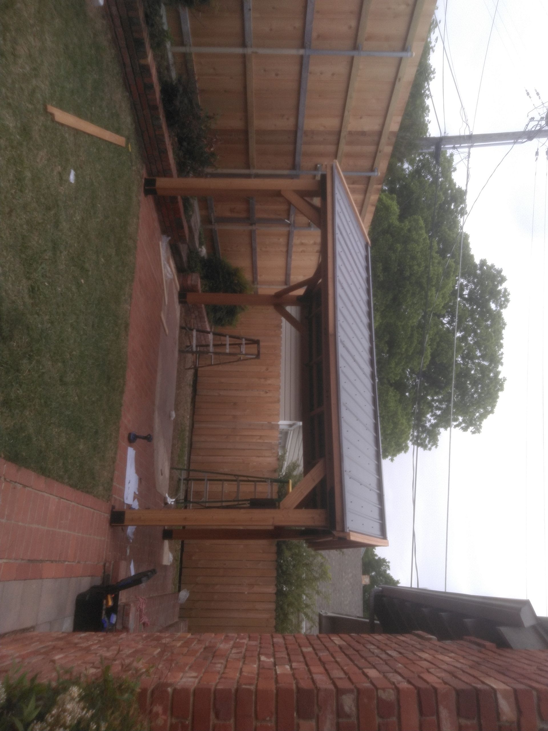 A wooden structure is being built in a backyard next to a brick wall.