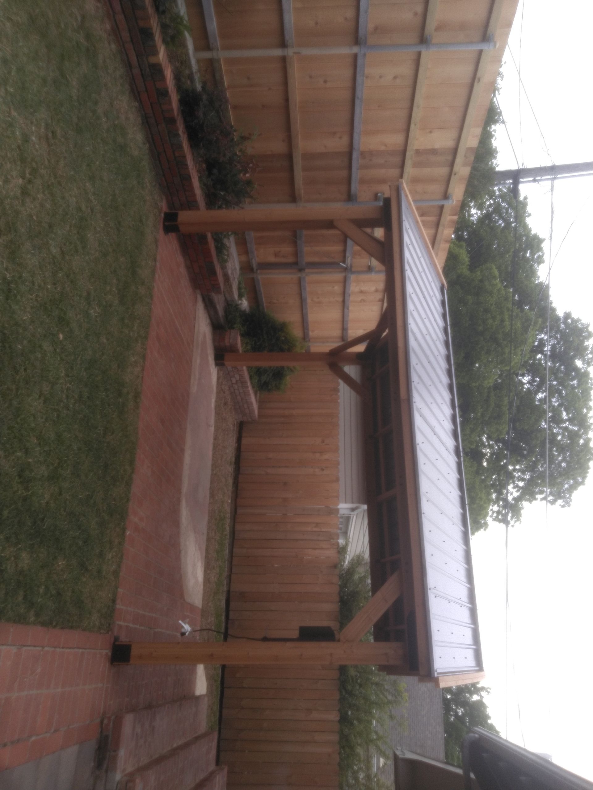A wooden pergola with a metal roof is in the backyard of a house.
