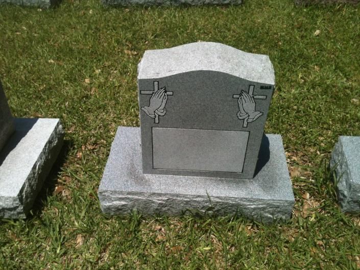 Gray gravestone with blank plaque and small angel carvings on a grassy lawn