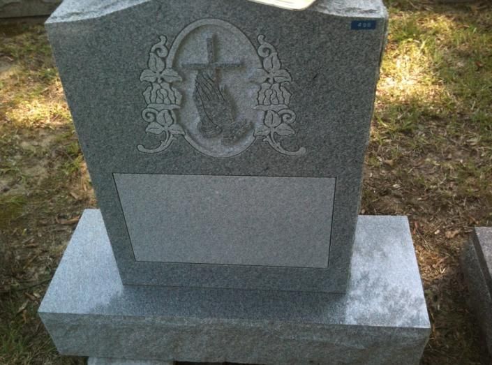 Gray granite gravestone with an engraved cross and blank plaque, in a cemetery outdoors