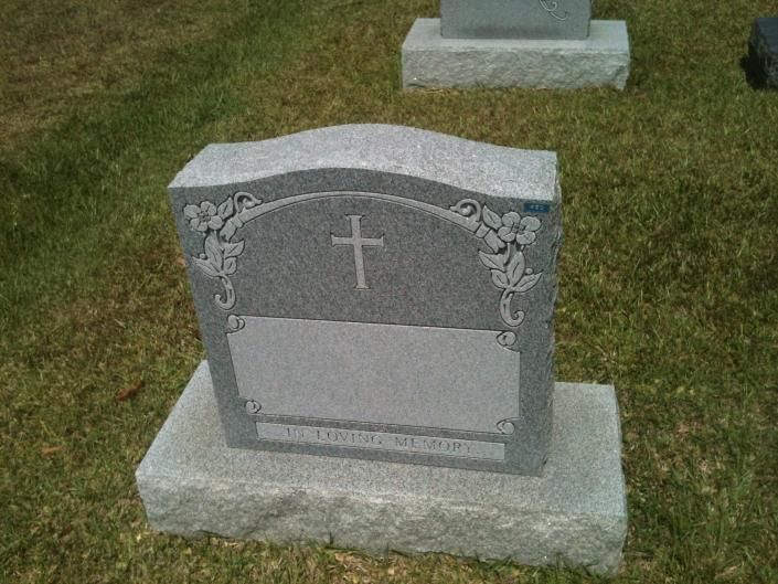 Gray granite gravestone with a cross and floral carvings on a grassy cemetery plot