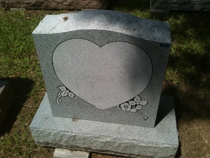 Gray heart-shaped gravestone with floral carvings on a grassy lawn