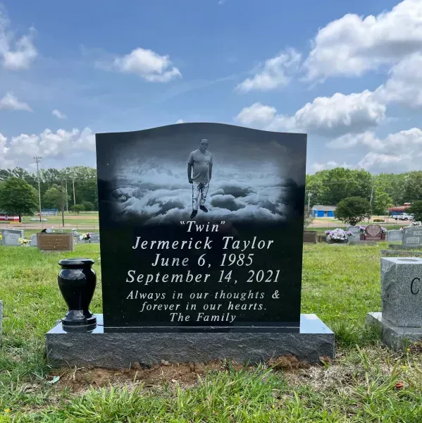 Black granite gravestone with photo and inscription in a cemetery under a cloudy sky