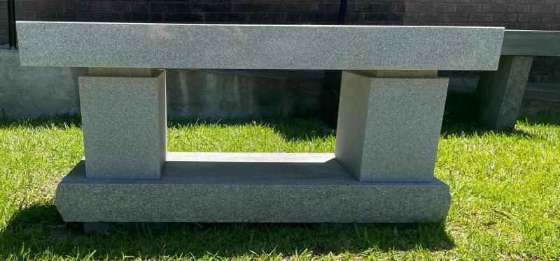 Gray concrete bench with a dark wooden top on a green lawn