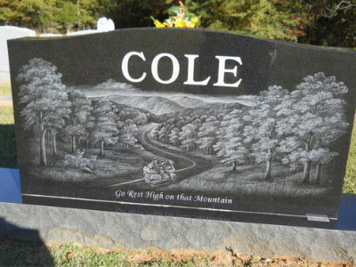 Black granite memorial stone engraved with “COLE” and a scenic valley and river etching.