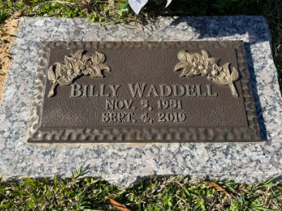 Gravestone for Billy Waddell with floral relief, set in a concrete border on grass.