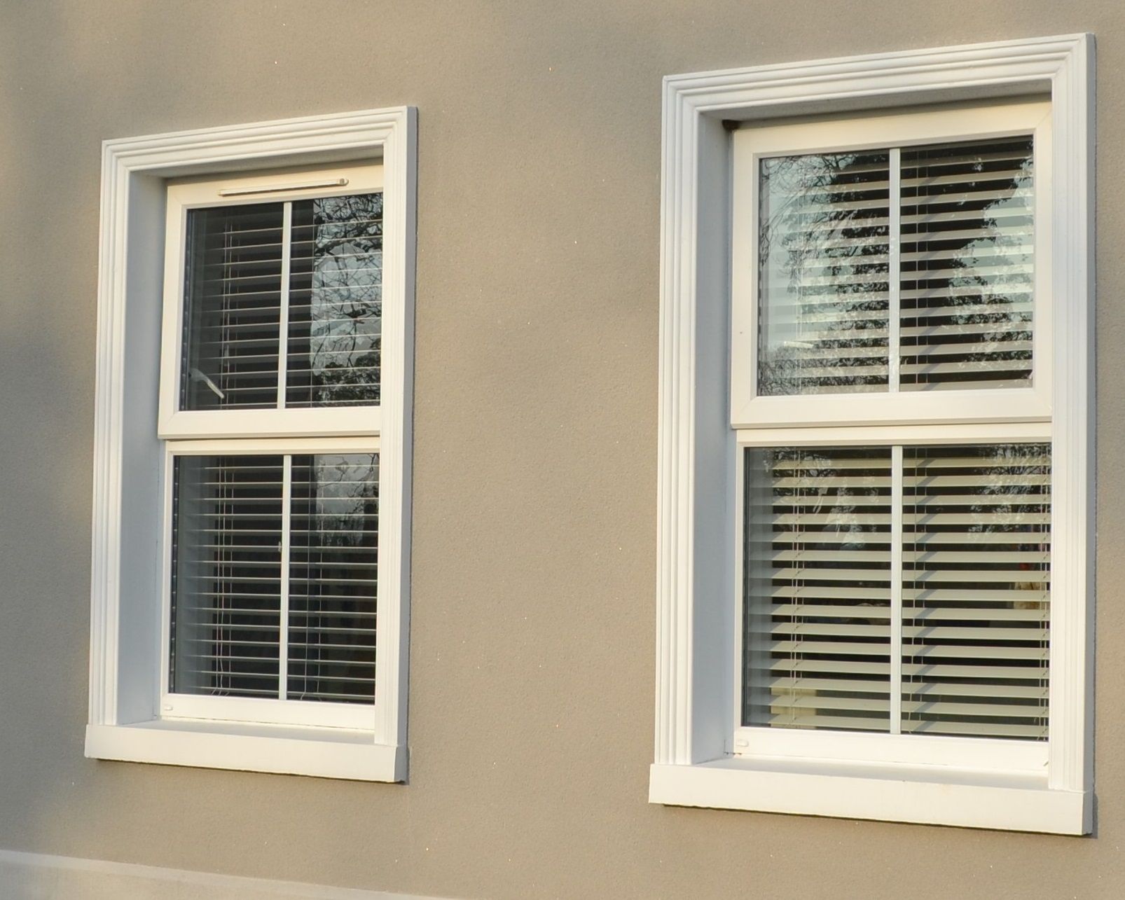 Two windows on the side of a house with blinds