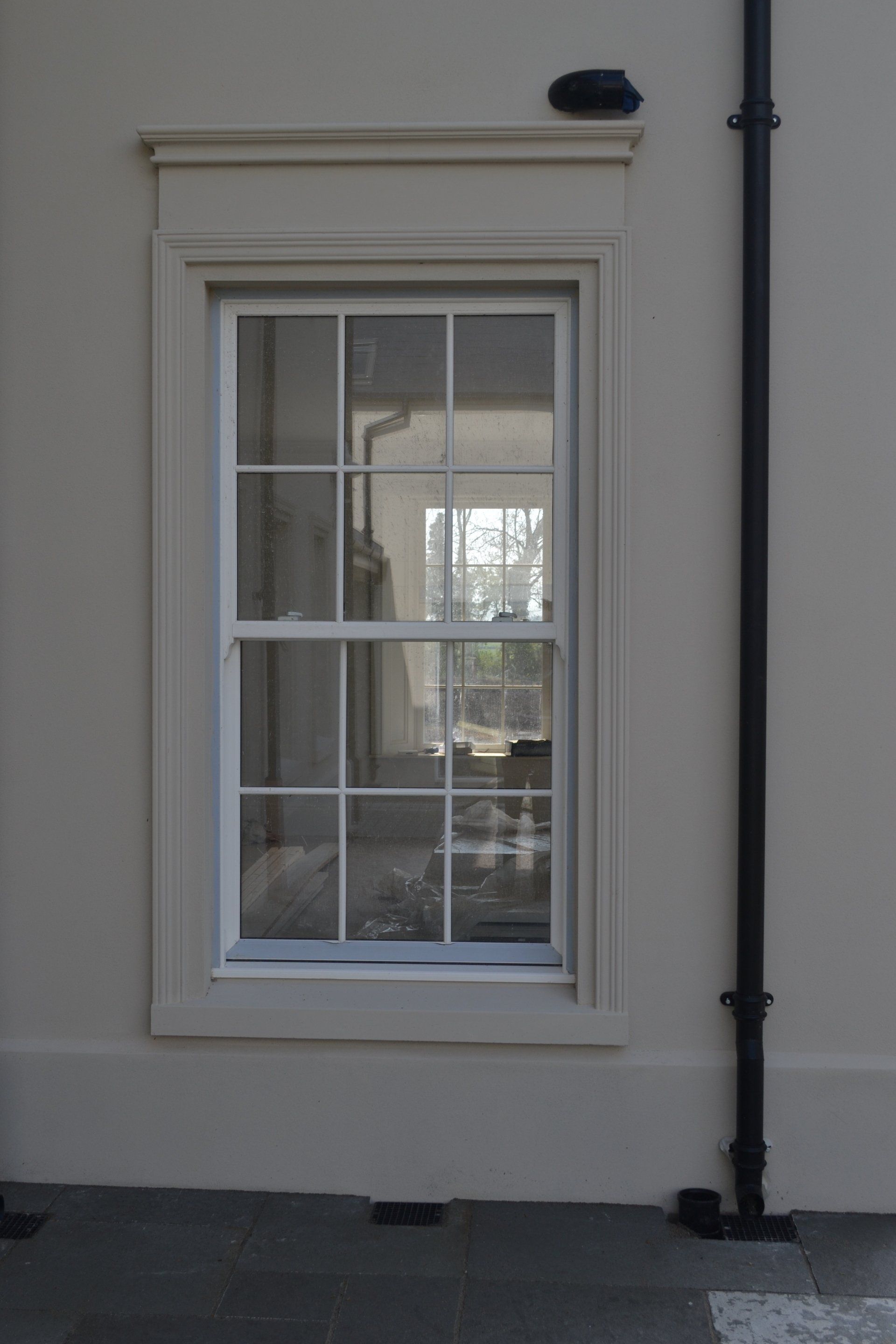 A window on the side of a building with a black pipe next to it.