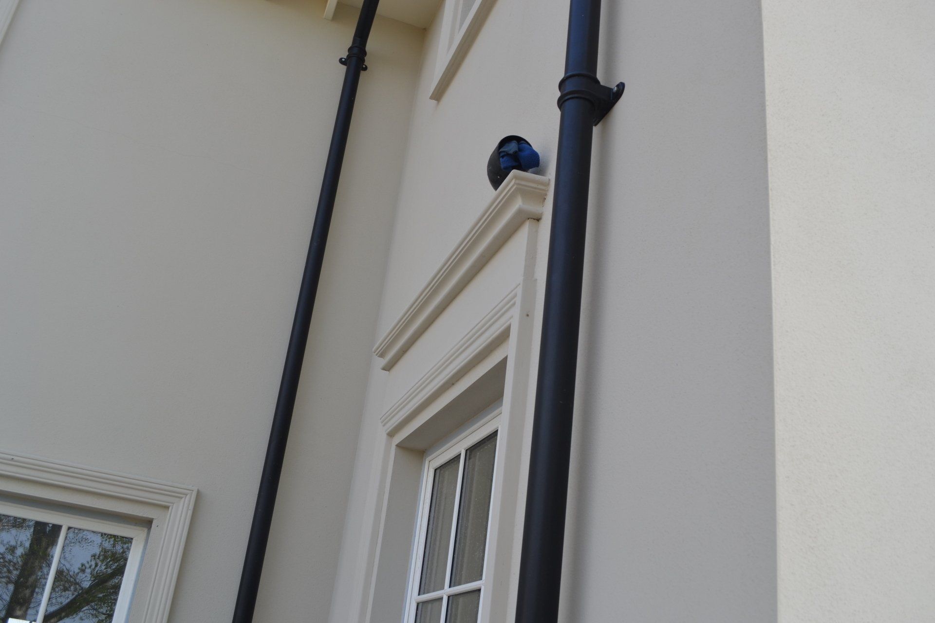 A black pipe is hanging from the side of a building next to a window.