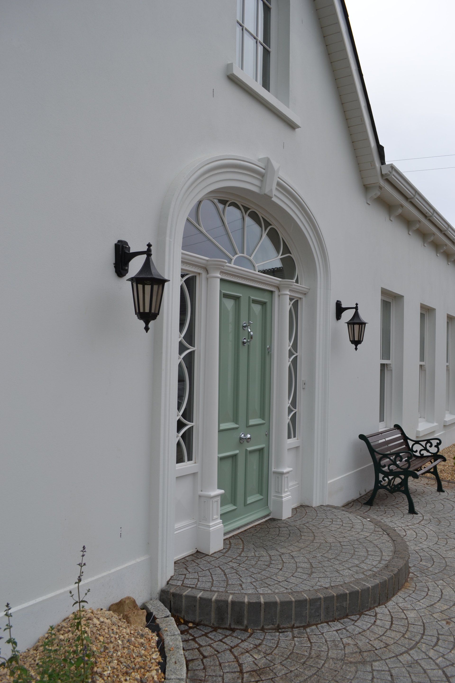 A white house with a green door and a bench in front of it.