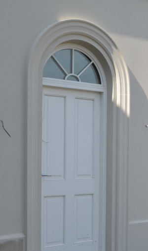 A white door with an arched window on the side of a building.