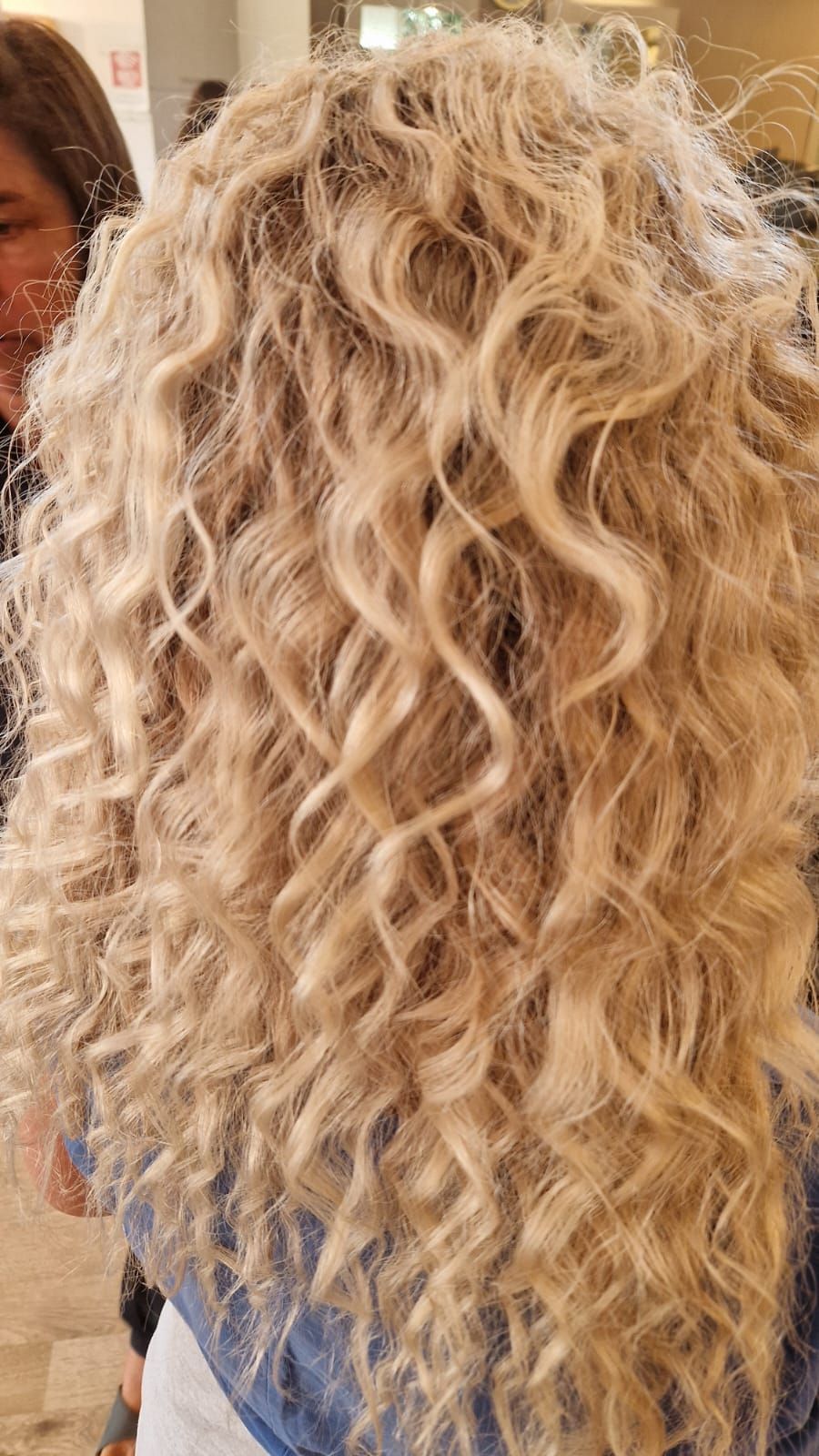 Capelli biondi e ondulati che scendono a cascata sulla schiena; in casa, luce naturale.