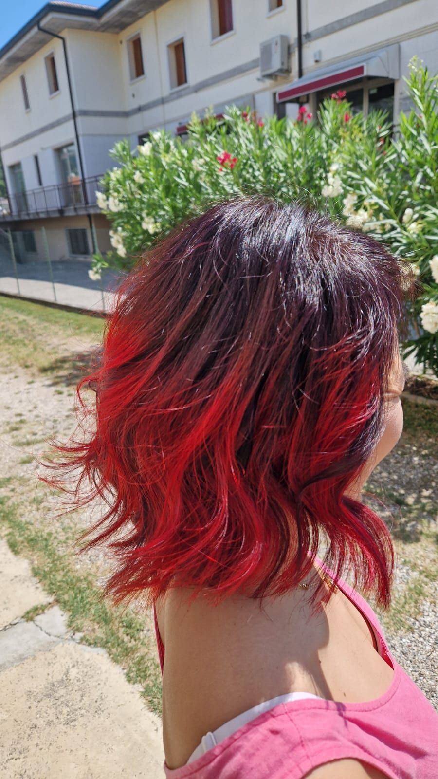 Donna con capelli ondulati e sfumati di rosso all'aperto, alla luce del sole.