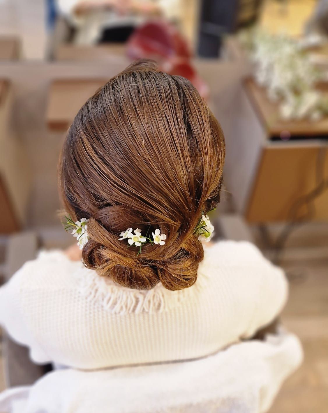 Donna con acconciatura intrecciata castana decorata con fiori bianchi, che indossa un maglione bianco.