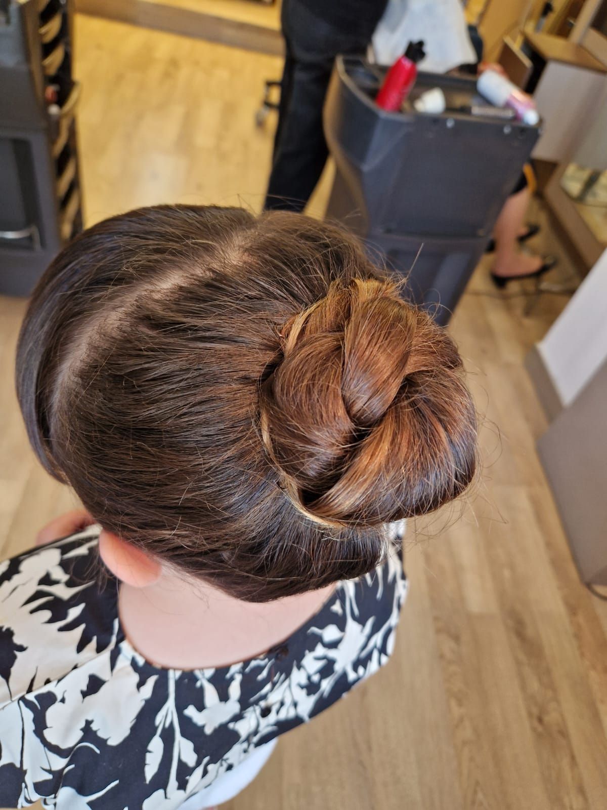 Persona con i capelli castani raccolti in uno chignon intrecciato, che indossa una camicia a fantasia bianca e nera, in un salone di bellezza.