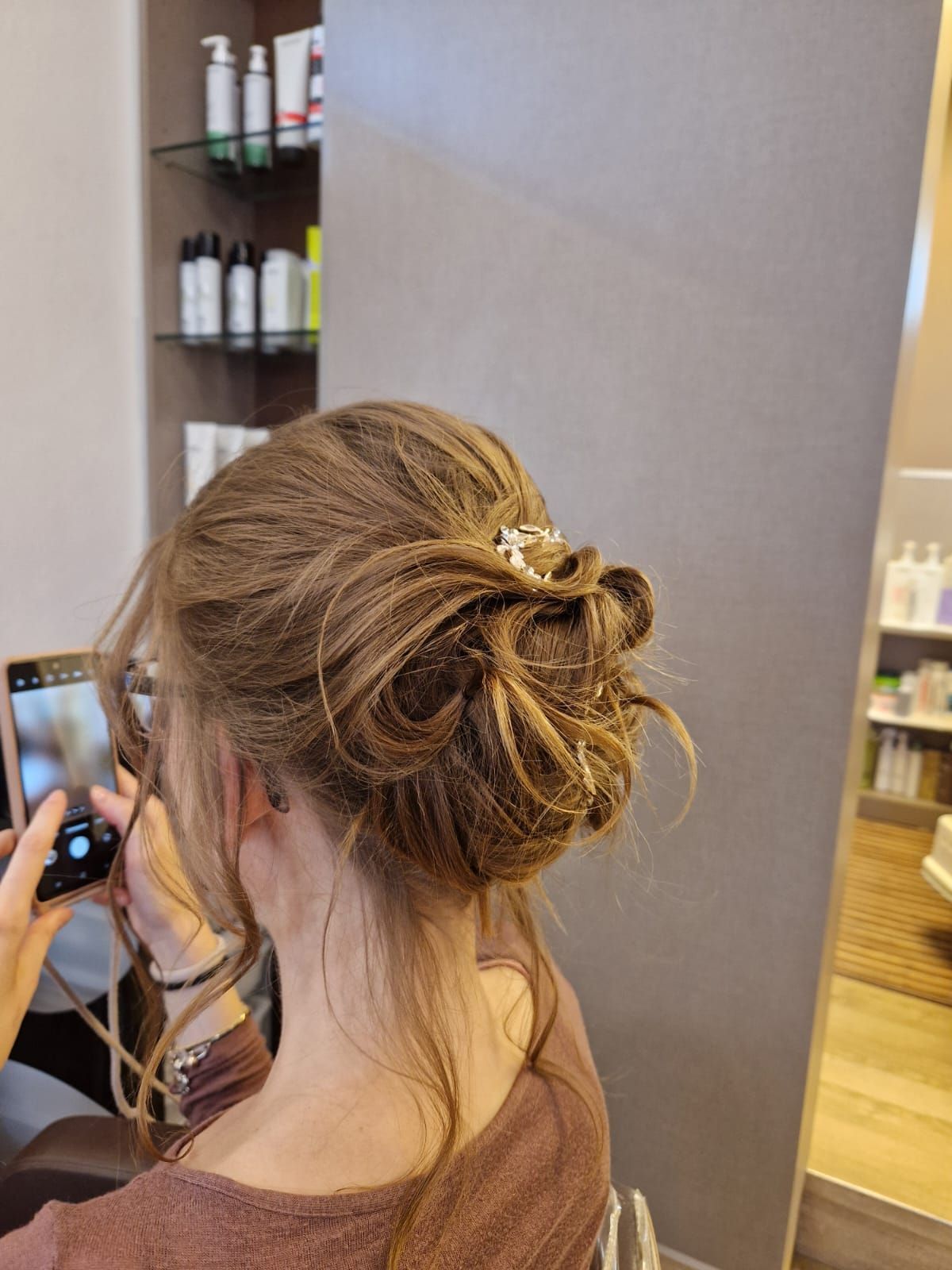 Capelli raccolti da una donna con una molletta decorativa. Qualcuno scatta una foto con uno smartphone in un salone di bellezza.