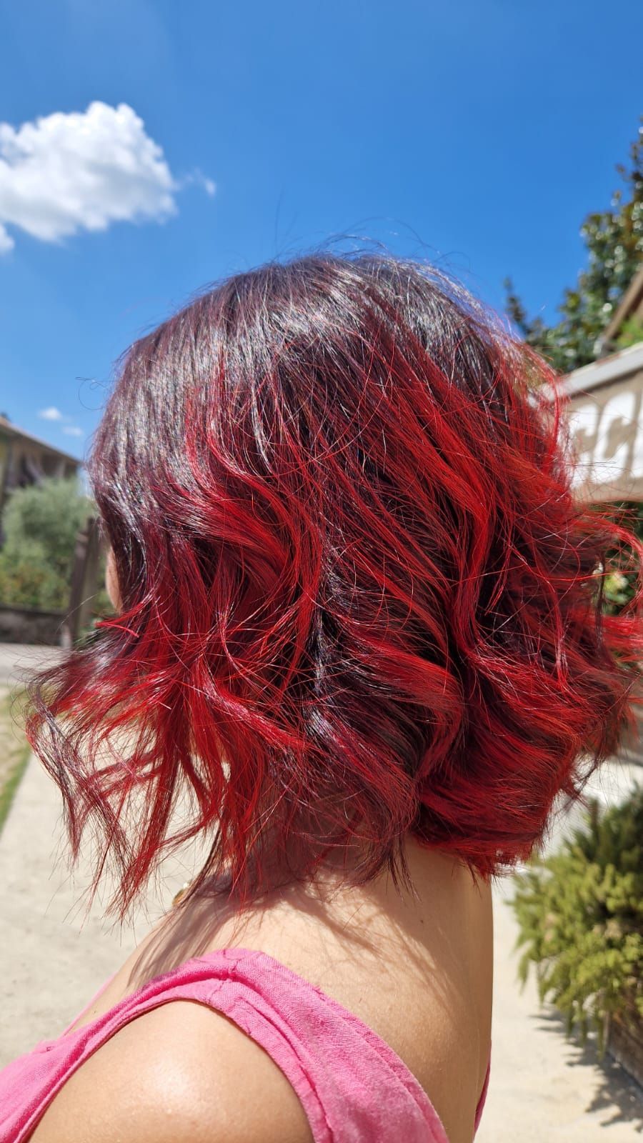 Donna con capelli rosso scuro con una vibrante sfumatura rossa, all'aperto in una giornata di sole.