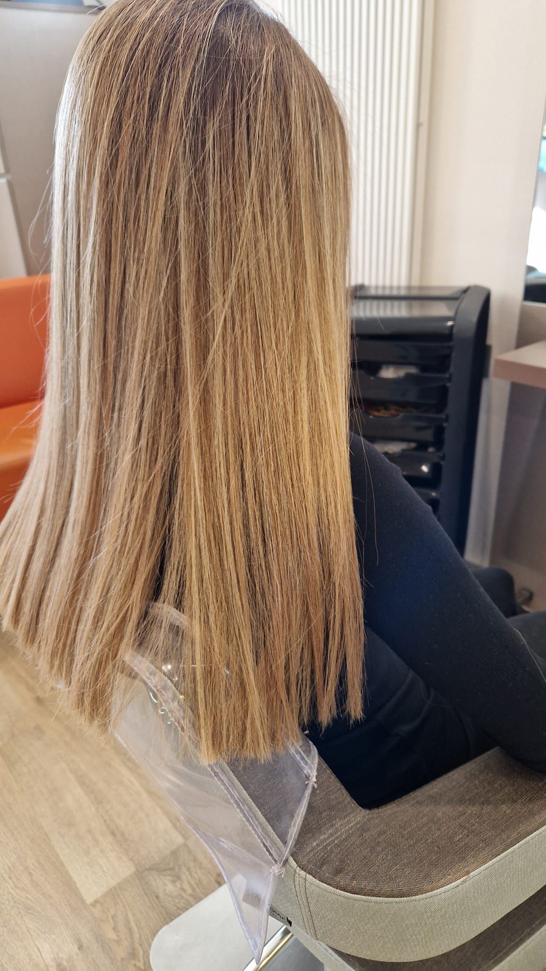 Donna con lunghi capelli biondi e lisci seduta su una sedia.