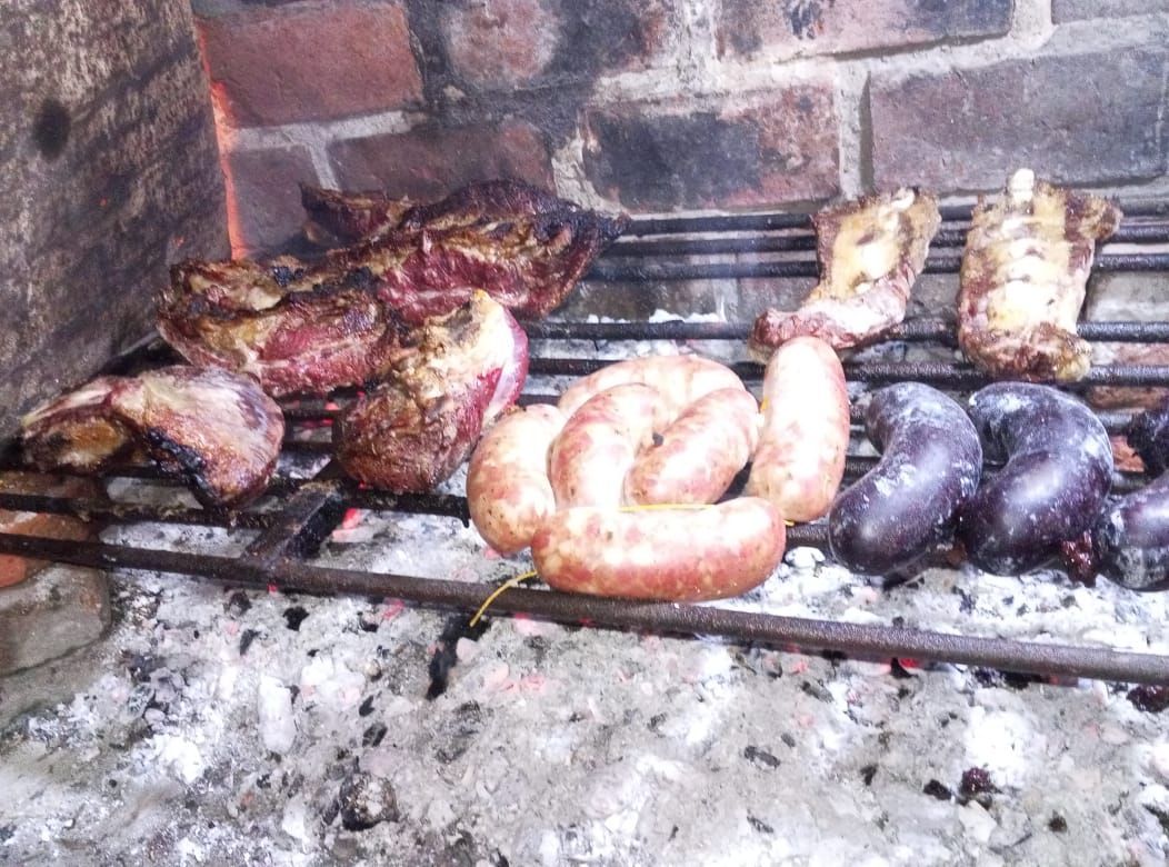 Parrilla con diversas carnes: bistec, chorizos y morcillas, cocinadas sobre brasas calientes.