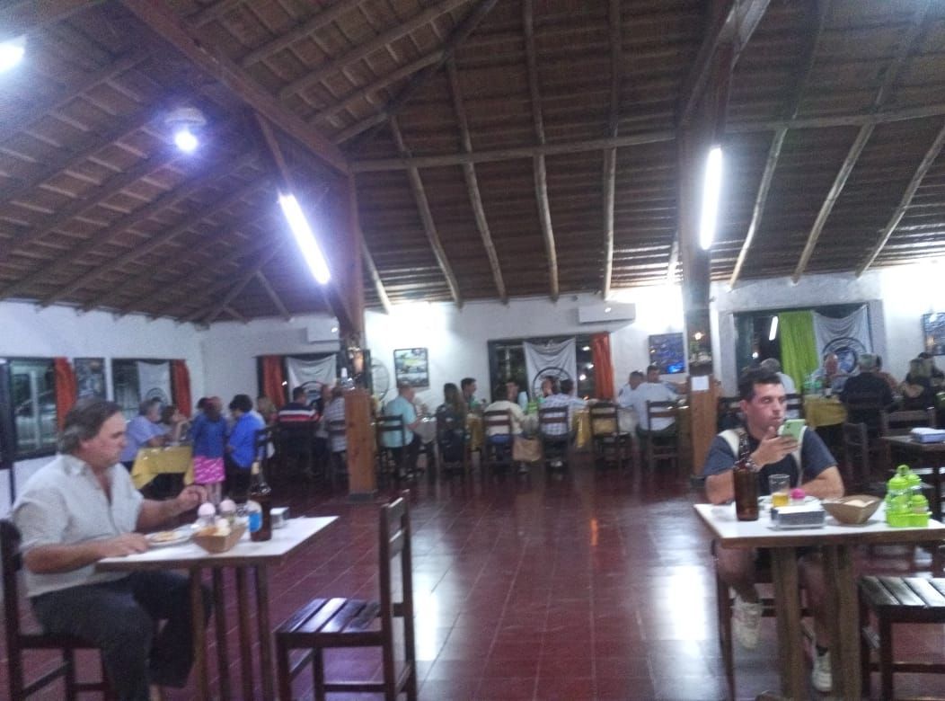 Interior de un restaurante con gente sentada en mesas, sillas de madera y techo de paja.
