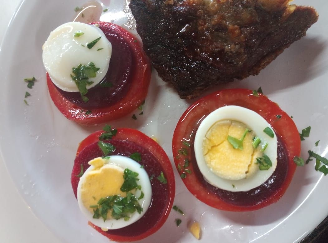 Aperitivo de tomate, remolacha y huevo con pescado a la parrilla en un plato blanco.