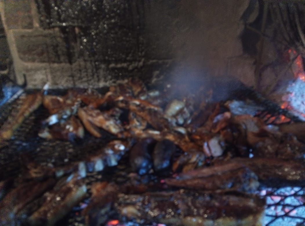 Carne asándose sobre una rejilla metálica. Sale humo.