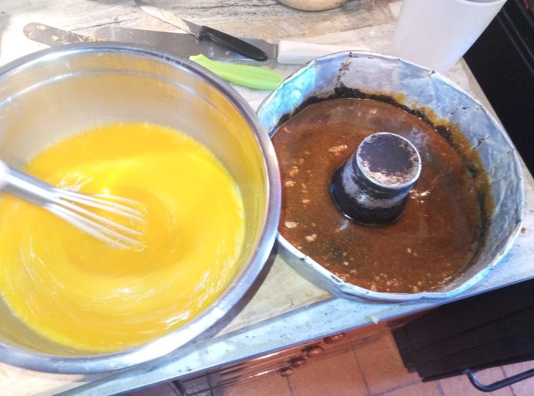 Cuenco con masa amarilla y batidor, al lado de un molde Bundt con masa.