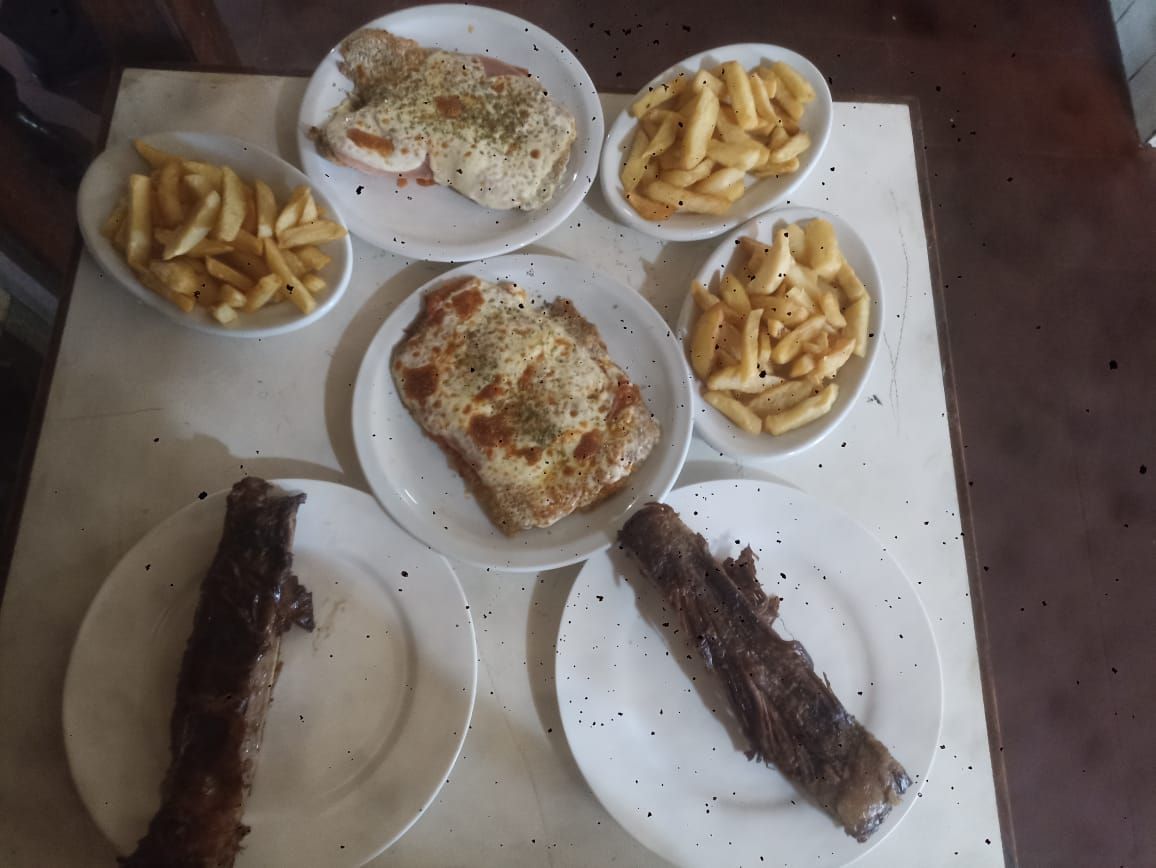 Platos de carne, papas fritas y pollo empanizado se encuentran sobre una mesa, listos para ser comidos.