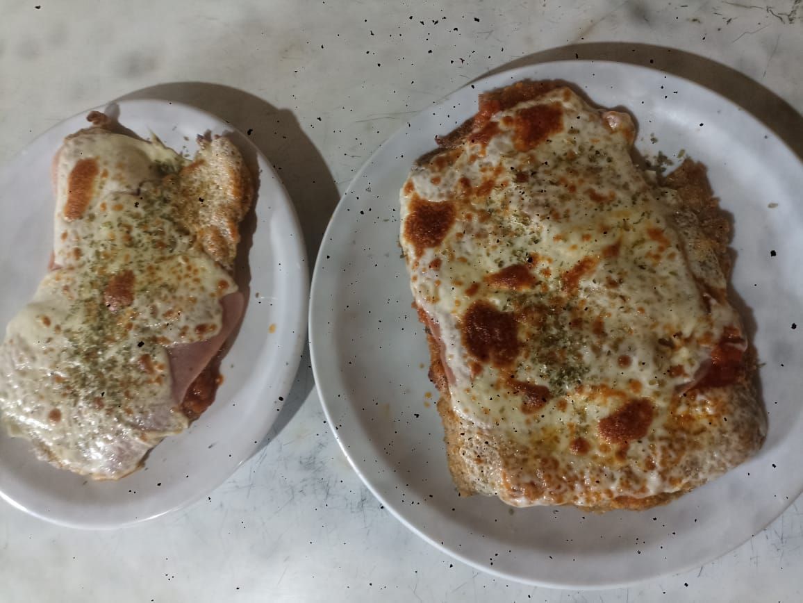 Dos platos de sándwiches abiertos con queso derretido, salsa de tomate y hierbas.
