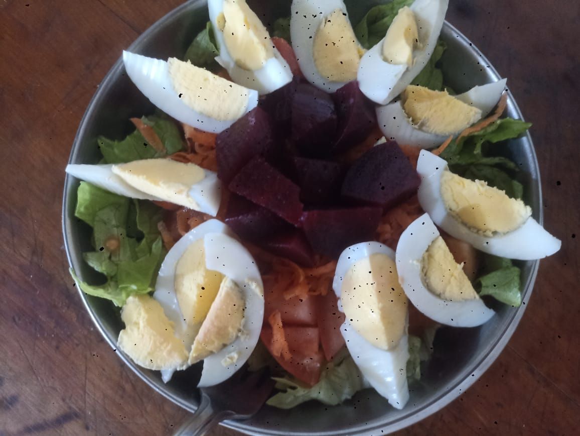 Ensalada en un recipiente de metal con huevos duros en rodajas, remolacha y lechuga sobre una superficie de madera.