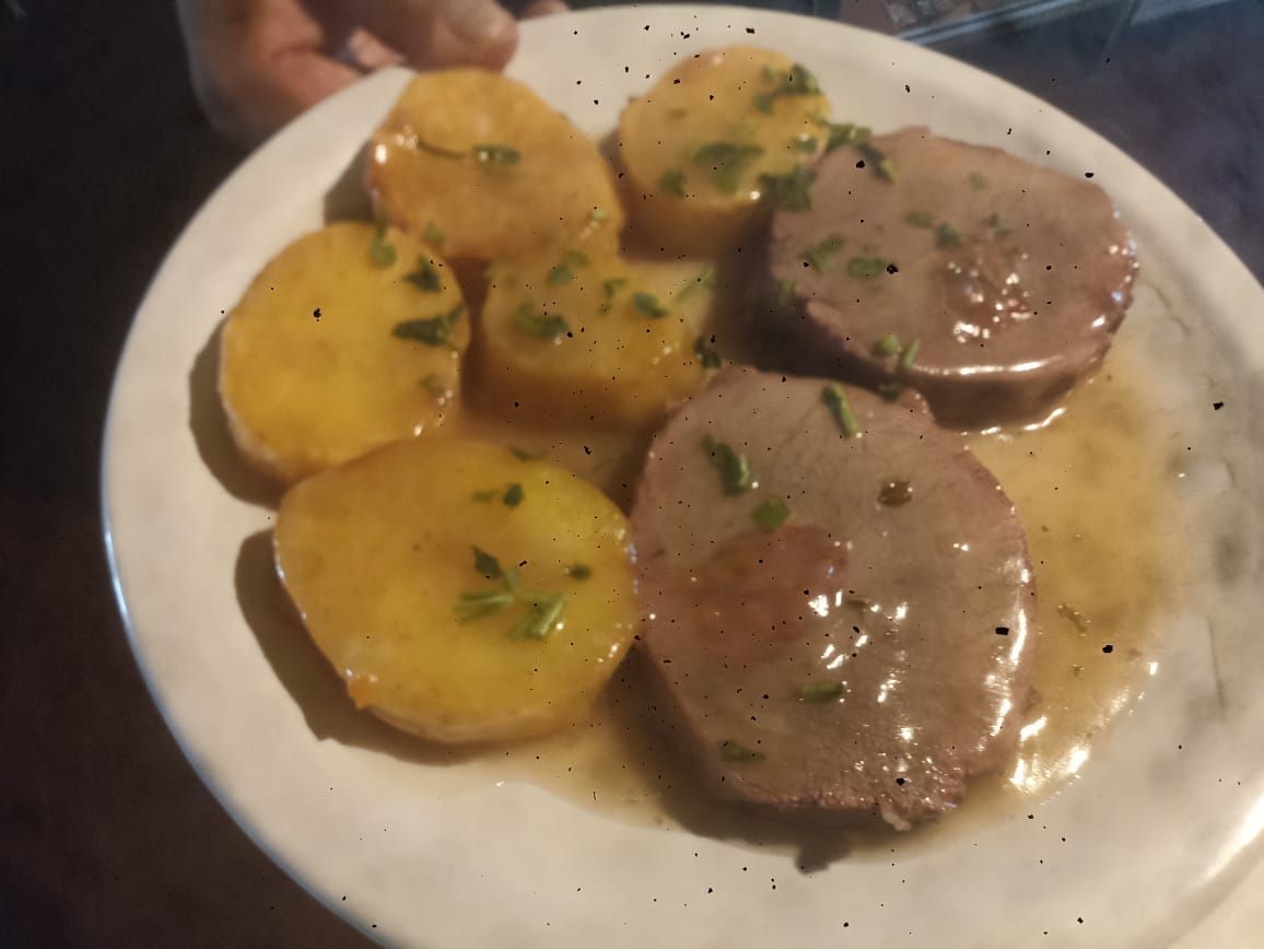 Plato de carne cortada en rodajas y patatas en salsa, adornado con hierbas.