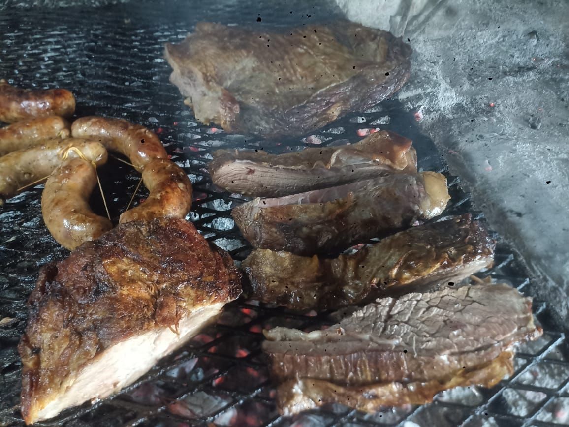 Carnes a la parrilla: salchichas, filetes y un gran asado cocinándose sobre parrilla de carbón.