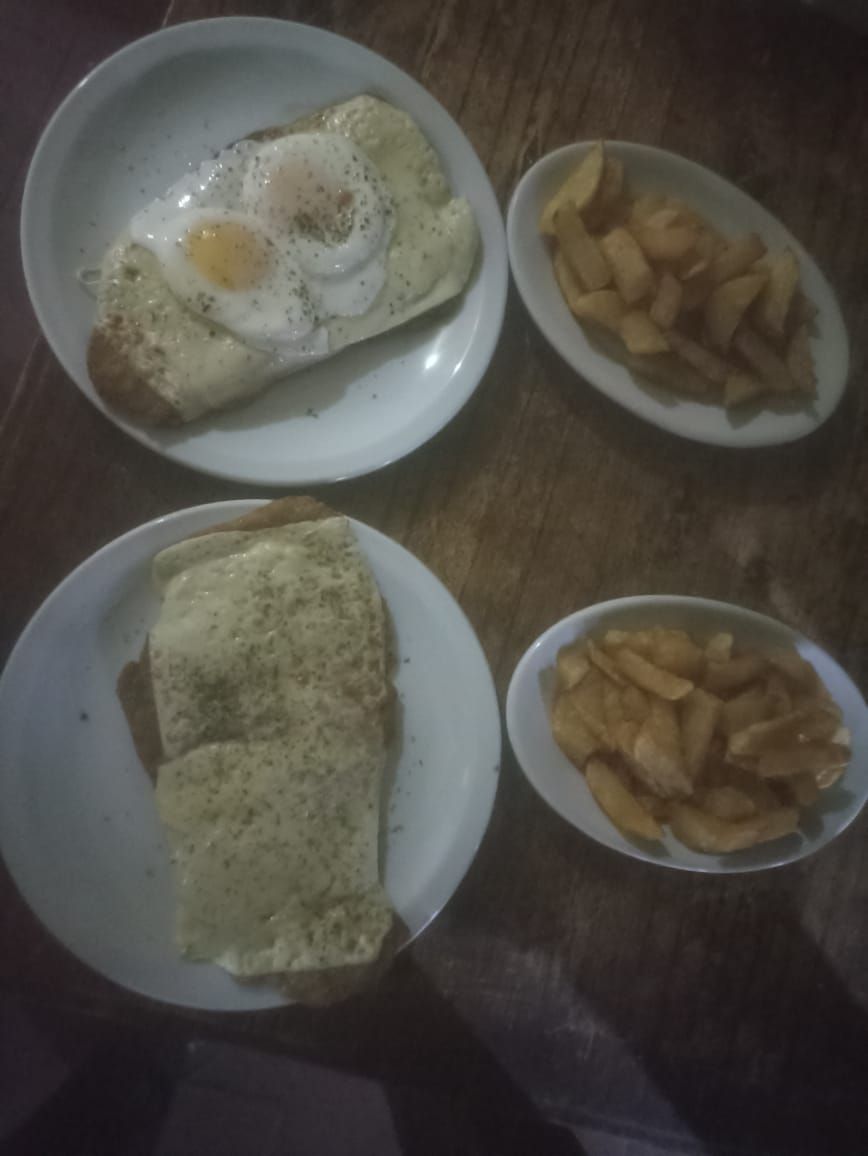 Dos platos de comida: sándwiches con queso y huevo frito encima, con dos raciones de patatas gajo.