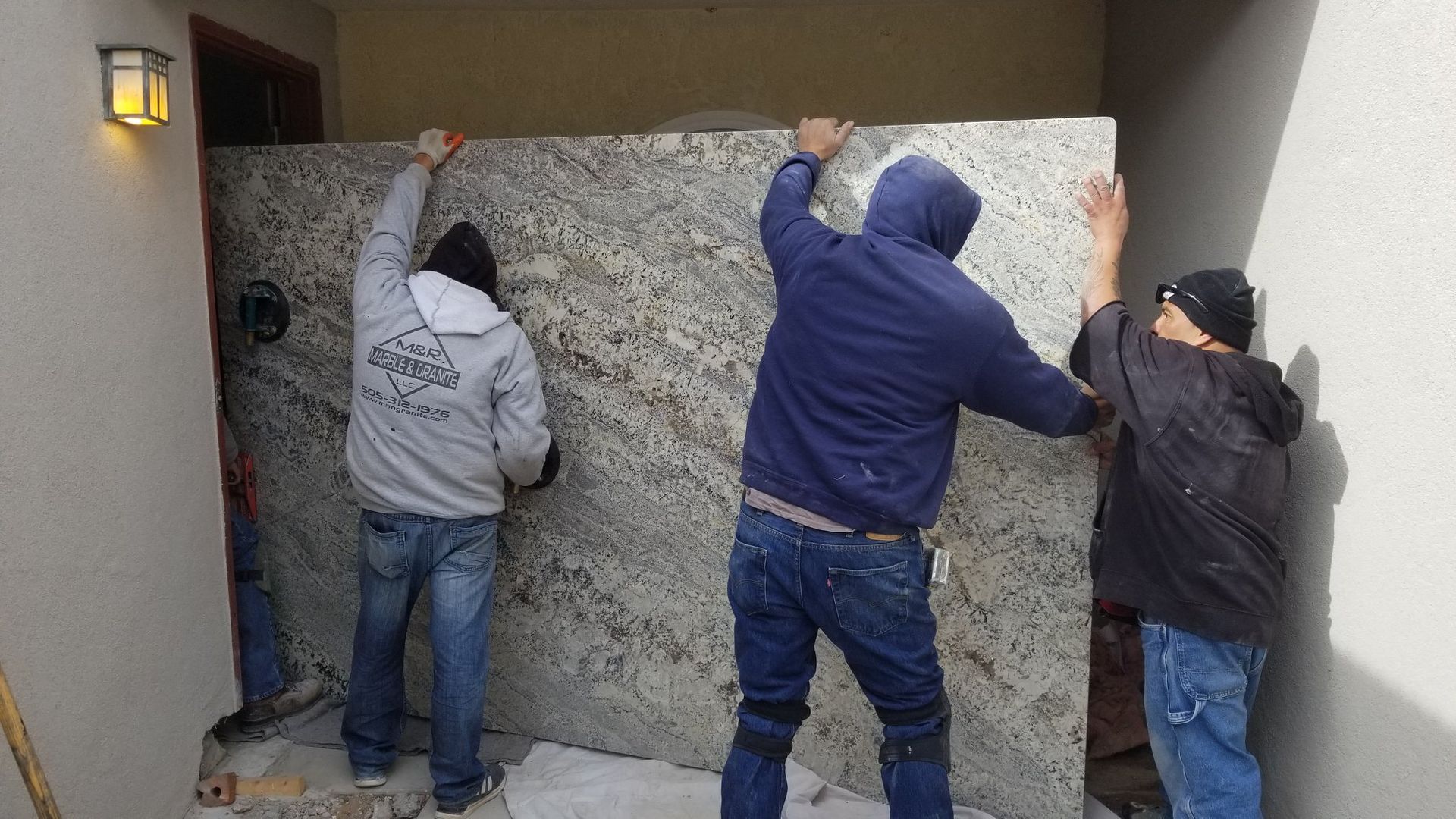 Three men are standing next to each other holding a large piece of granite.