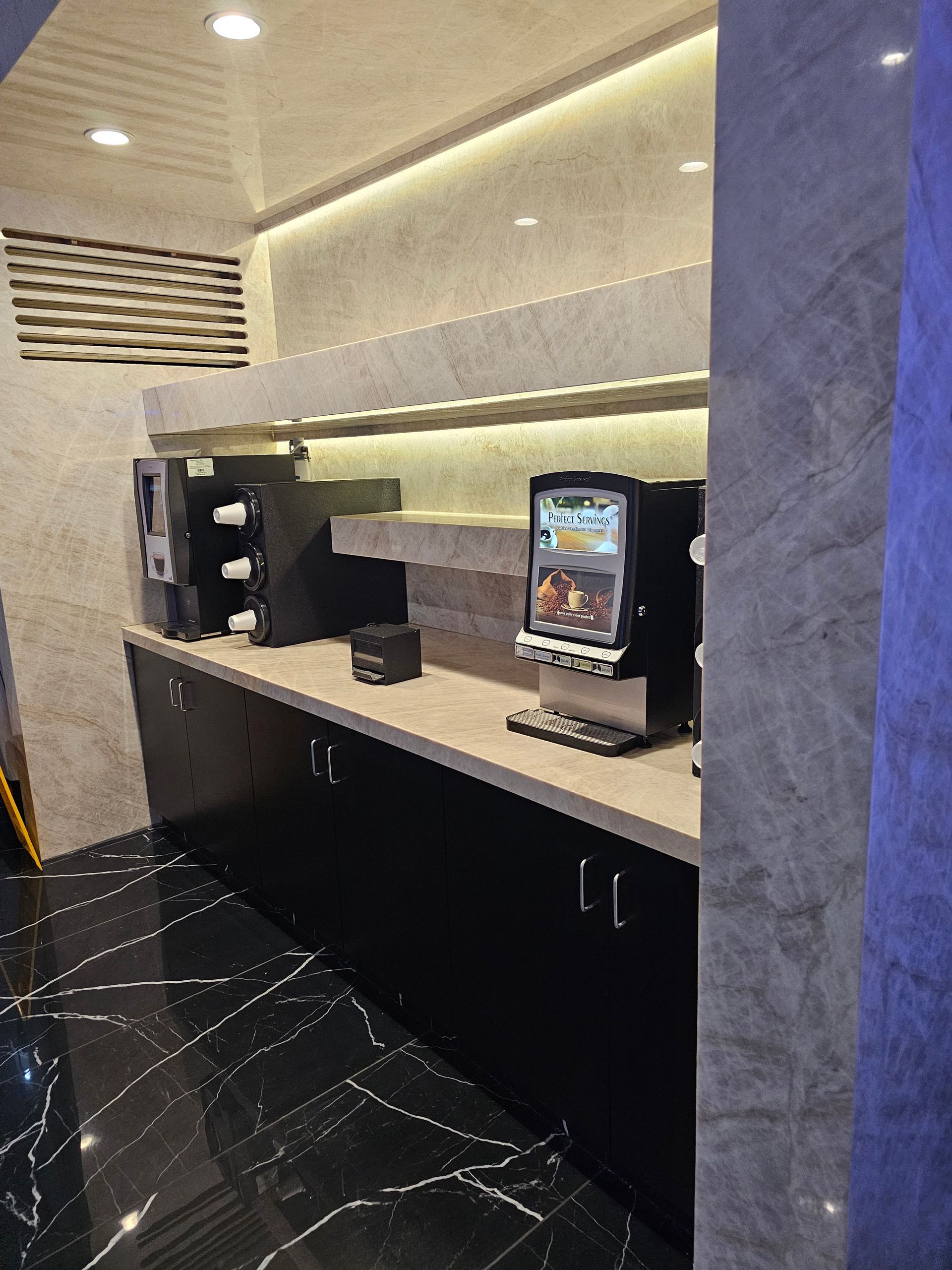 Coffee station with black cabinets, gray countertops, and coffee machines. The floor is black and white marble.