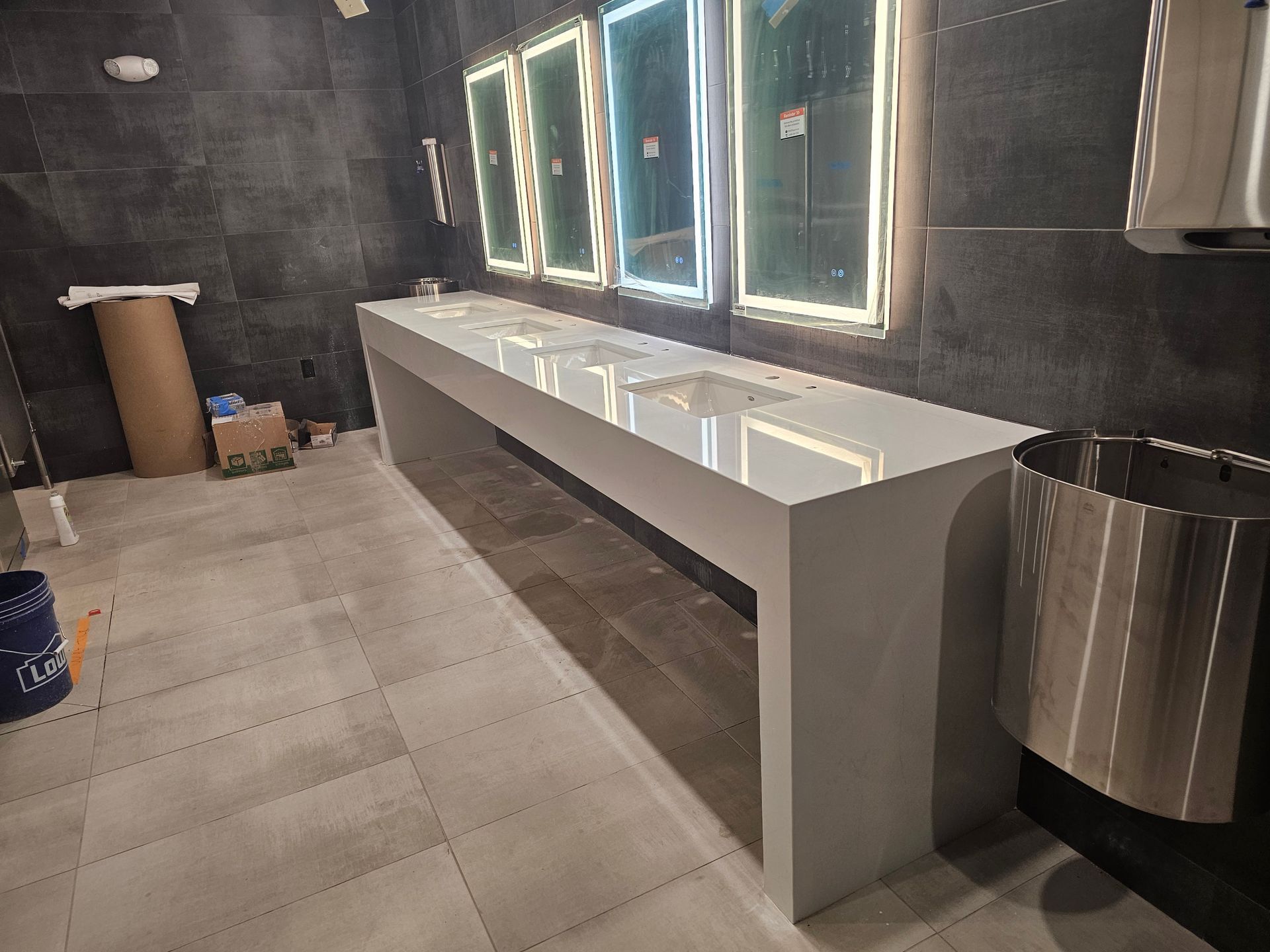 A modern bathroom with a long, white sink counter, three lit mirrors, and a trash can.