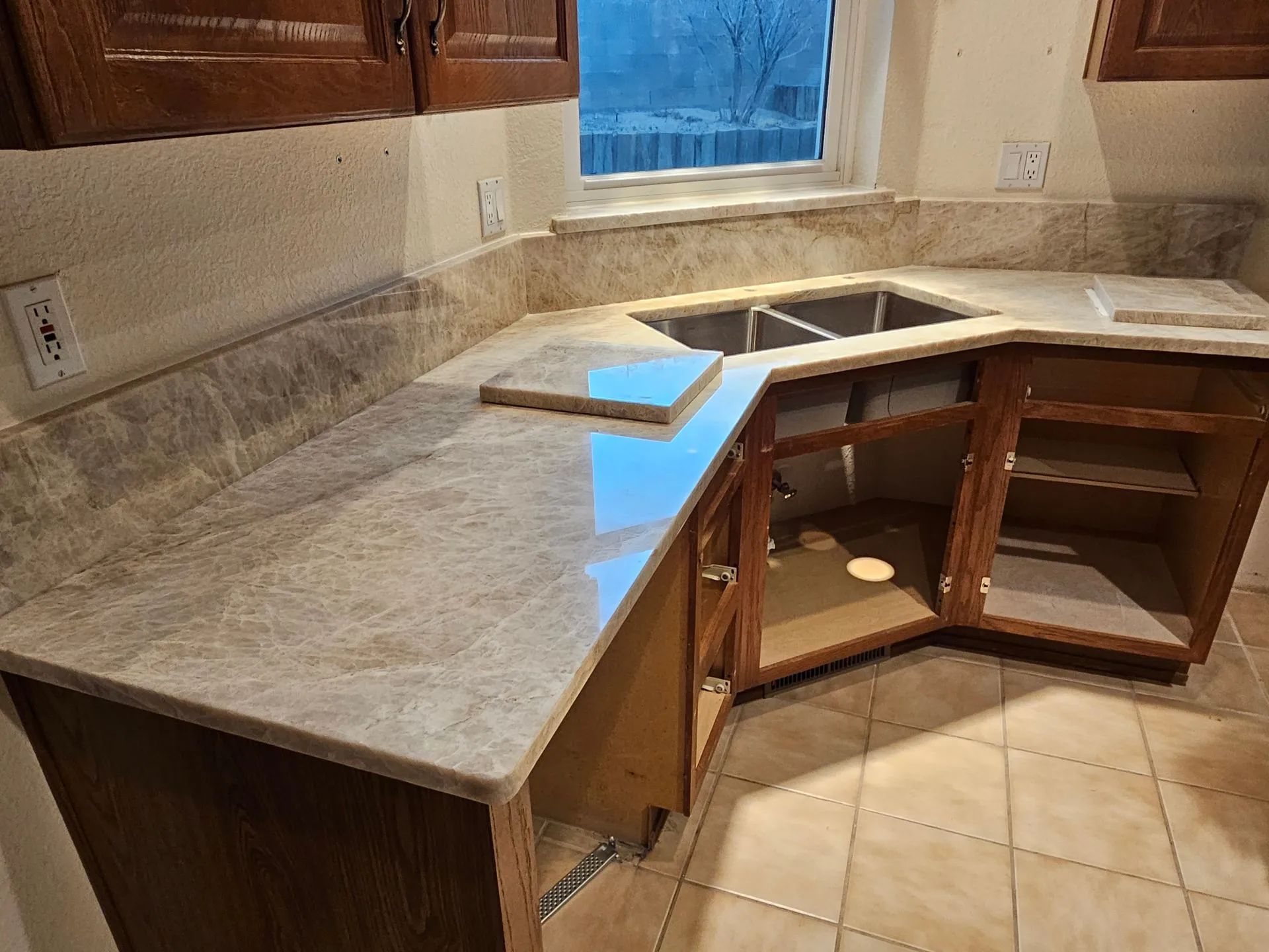 A kitchen with a sink , counter top , cabinets and tile floor.