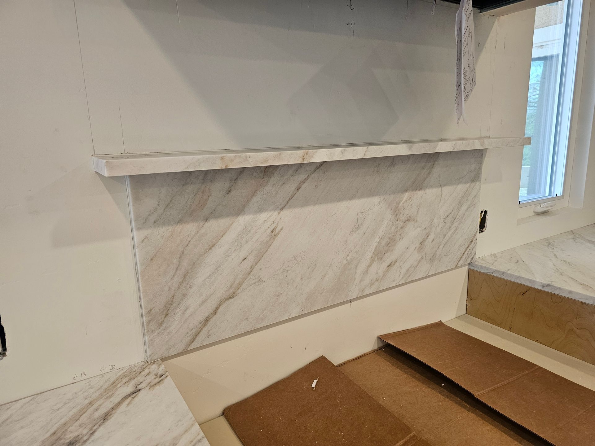 Wall with beige tile and shelf installed, next to a window.