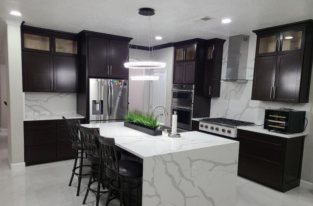 A kitchen with black cabinets and white counter tops and a large island.