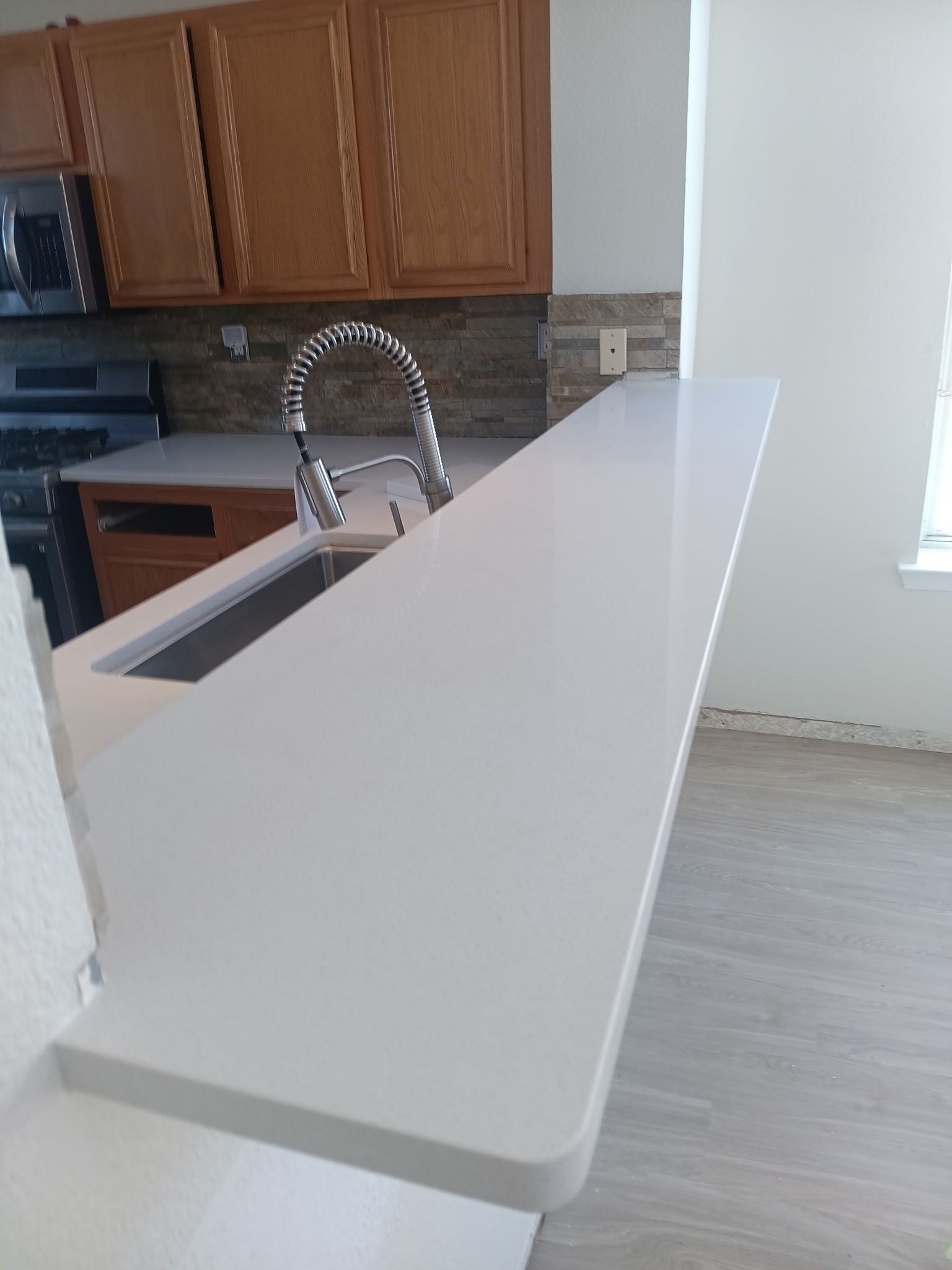 White countertop with a built-in sink and faucet; light brown cabinets above and a stone backsplash.