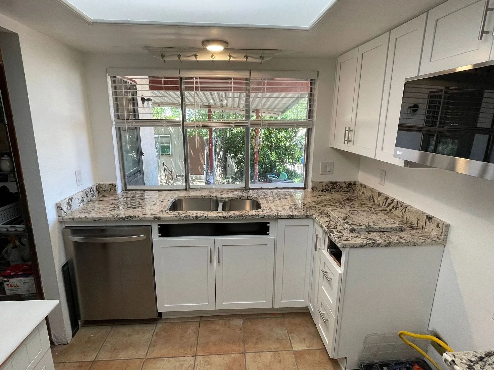 A bright kitchen with white cabinets, speckled granite countertops, a stainless steel dishwasher, and a large window.